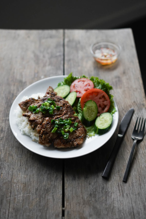 a plate of Vietnamese pork chops and rice, with tomato, cucumber and fish sauce